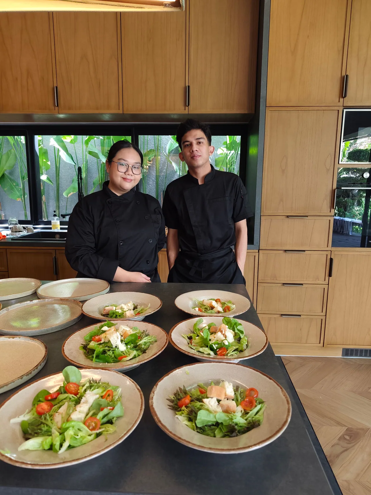 Two chefs standing behind plates of salad in a villa kitchen